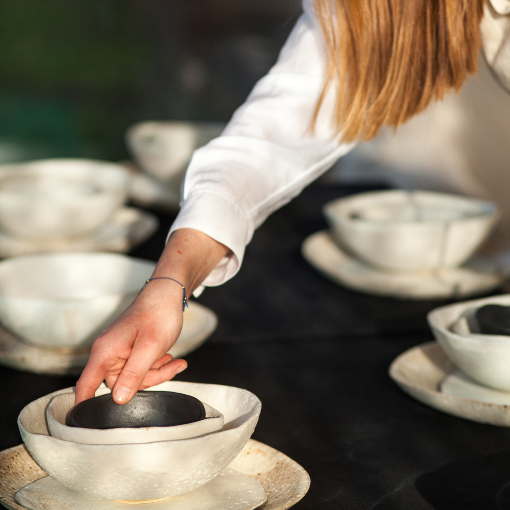 stół zastawiony ceramicznymi naczyniami. Kobieca ręka sięga po miskę. Pracownia Moja Siostra
