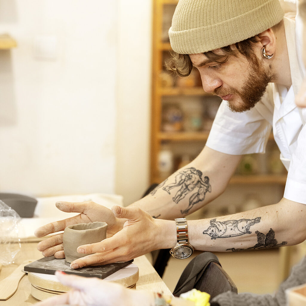 Wytatułowany chłopak lepi czarkę ceramiczną.